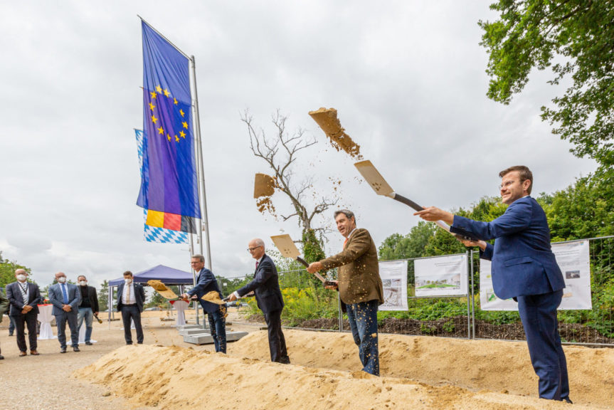 Dr. Söder, Marcus König, Prof. Hans Jürgen Prömel und Bernd Sibler werfen mit den Spaten Erde in die Luft. Im Hintergrund ist die EU, die deutsche und die bayerische Fahne zu sehen.