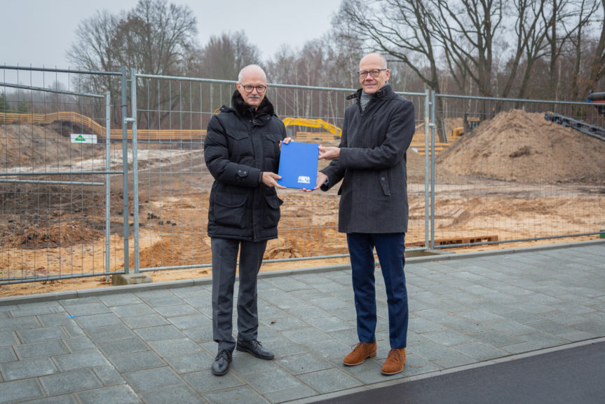 Die beiden Präsidenten stehen vor einem Bauzaun und halten gemeinsam eine blaue Mappe.