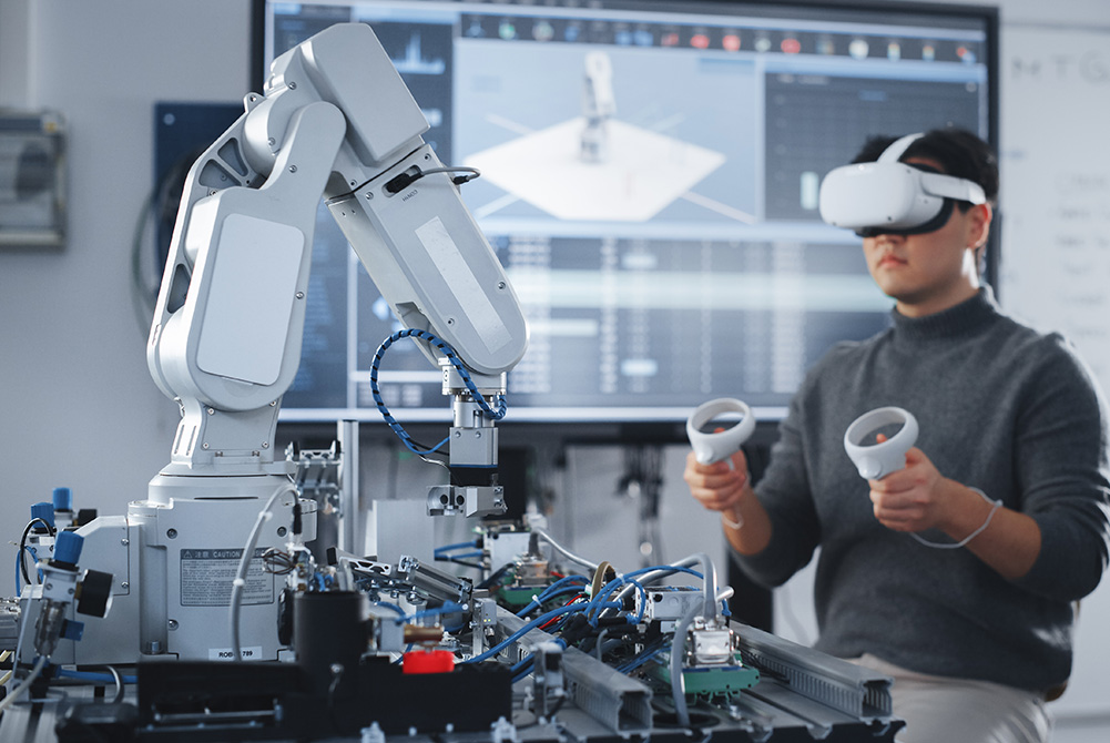 Ein Mann steuert einen Roboterarm. Dazu trägt er eine VR-Brille und Controller.