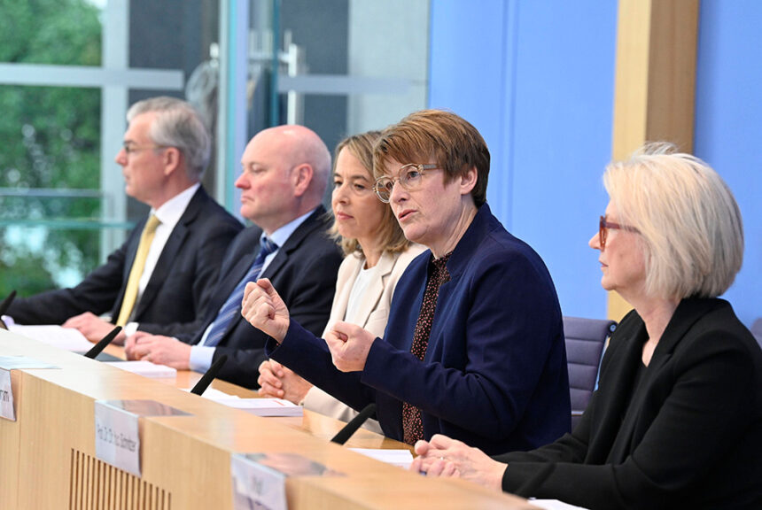 Die vier Wirtschaftsweisen bei einer Pressekonferenz. Frau Grimm spricht und gestikuliert.
