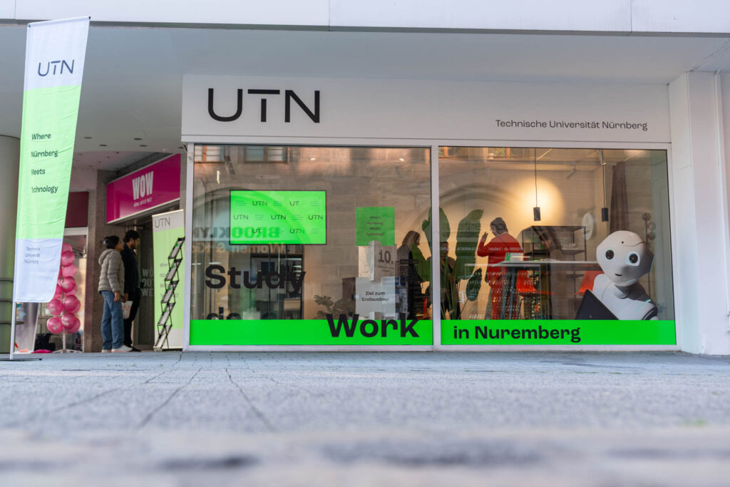 Das Schaufenster der UTN Science Lounge. Auf dem Fenster sind verschiedene Schriftzüge und ein Roboter zu sehen.