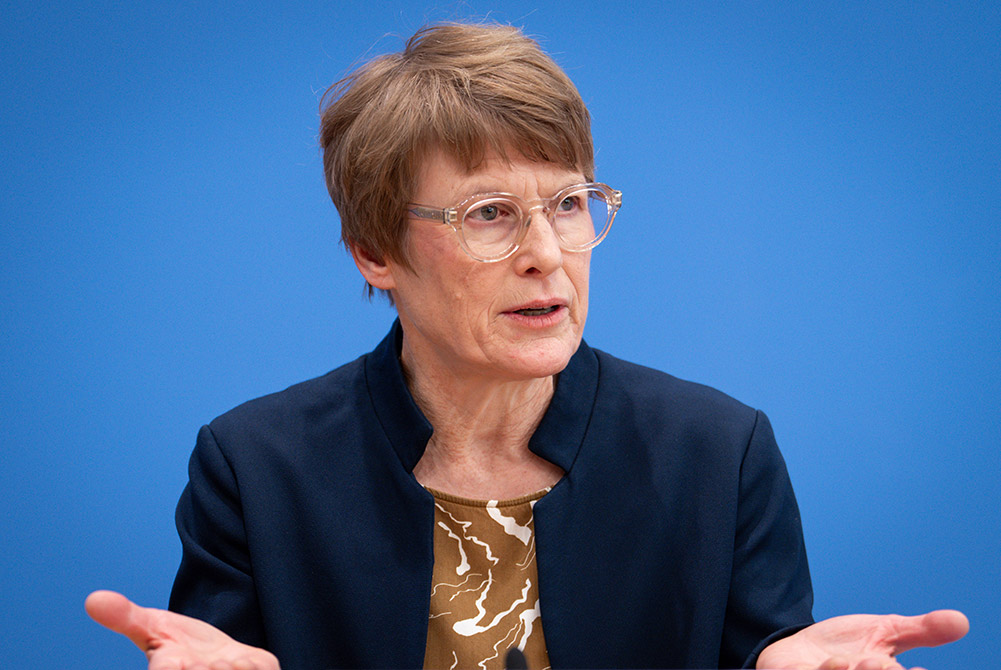 Mitglied des Sachverständigenrats Professorin Veronika Grimm spricht bei einer Pressekonferenz vor blauem Hintergrund und gestikuliert mit offenen Händen.