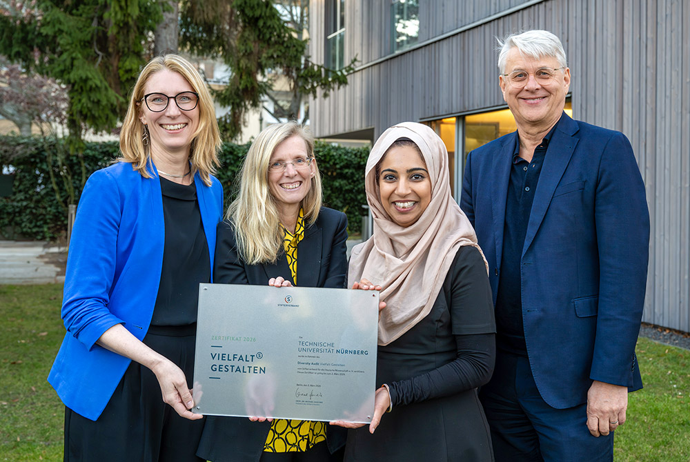 Vier Mitarbeitende der UTN stehen vor einem Gebäude und halten gemeinsam eine Zertifikatsplakette für das erfolgreich bestandene Diversity-Audit