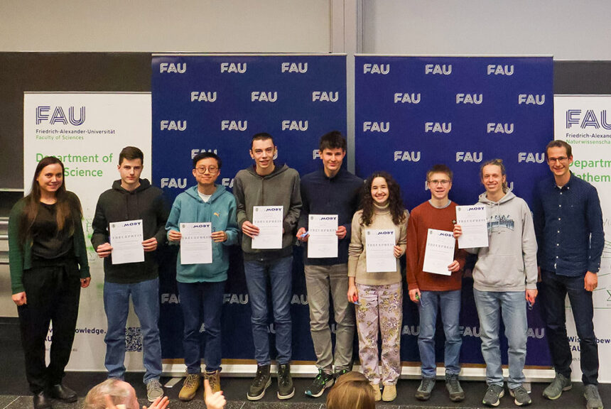 Ausgezeichnete Schülerinnen und Schüler der Mathematik-Olympiade an der FAU Erlangen stehen mit Betreuenden auf der Bühne; rechts steht ein Professor der UTN.