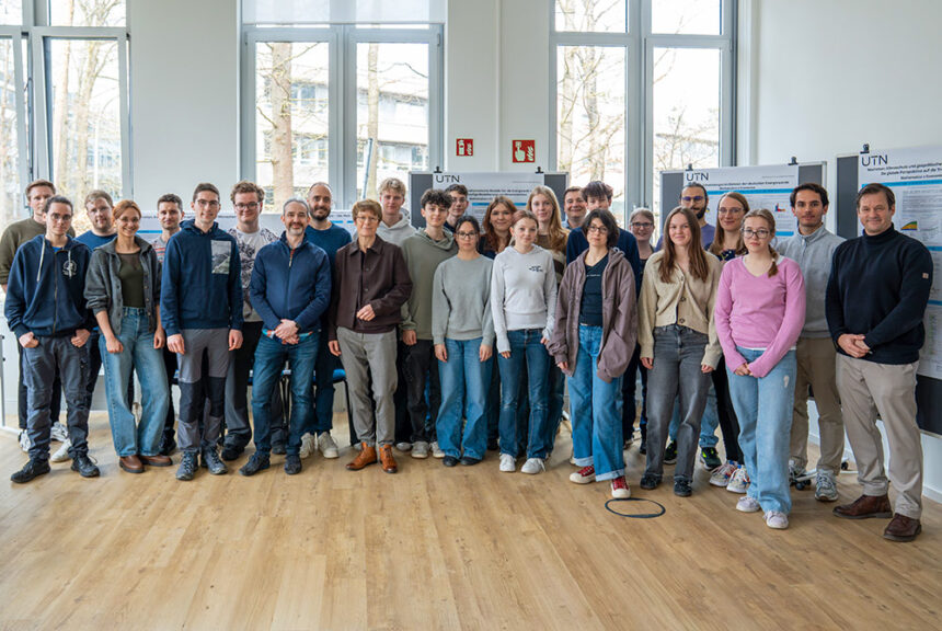 Gruppenfoto der Hochbegabtenklasse des Albrecht-Dürer-Gymnasiums Nürnberg bei einem Besuch in einem Hochschulgebäude vor wissenschaftlichen Postern.