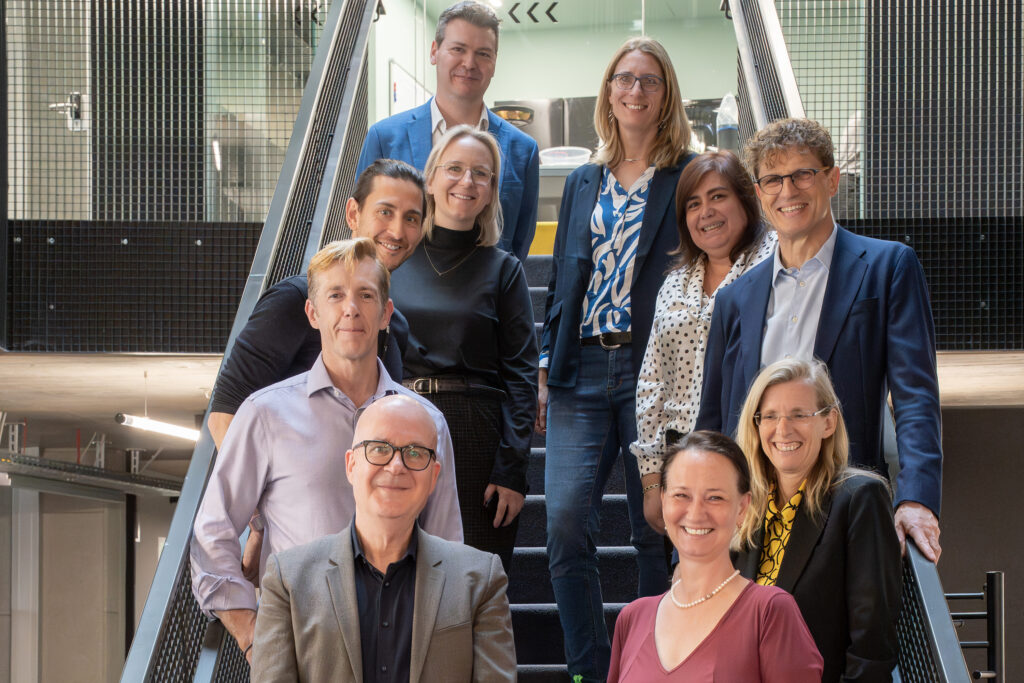 Gruppenfoto von zehn Personen auf einer Treppe in einem modernen Bürogebäude.